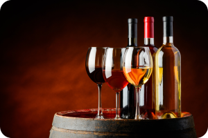 Três garrafas de vinho (uma tinto, uma rosé e uma branco) e três taças cheias de vinho (tinto, rosé e branco) dispostas sobre um barril de madeira rústico, com um fundo marrom escuro suavemente iluminado.